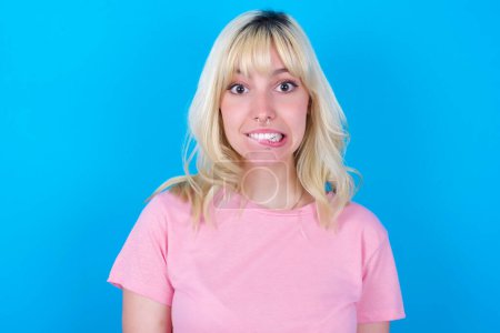 Photo for Caucasian girl wearing pink t-shirt isolated over blue background being nervous and scared biting lips looking camera with impatient expression, pensive. - Royalty Free Image