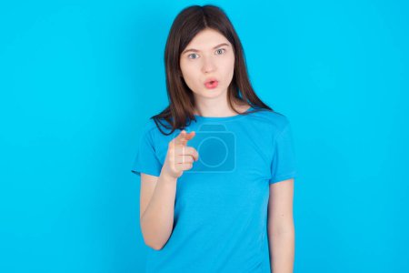 Téléchargez les photos : Choqué jeune fille caucasienne portant bleu T-shirt isolé sur fond bleu points à vous avec une expression stupéfaite - en image libre de droit