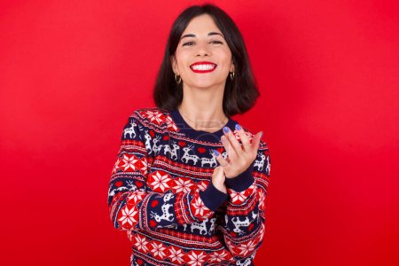 Téléchargez les photos : Brune caucasienne portant chandail de Noël sur fond rouge applaudissements heureux et joyeux, souriant mains fières ensemble. - en image libre de droit