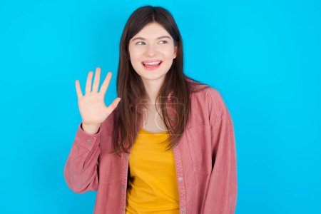 Téléchargez les photos : Jeune fille caucasienne portant chemise rose isolé sur fond bleu montrant et pointant vers le haut avec les doigts numéro cinq tout en souriant confiant et heureux. - en image libre de droit