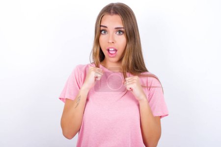 Photo for Portrait of desperate and shocked Young Caucasian girl wearing pink T-shirt on white background looking panic, holding hands near face, with mouth wide open. - Royalty Free Image