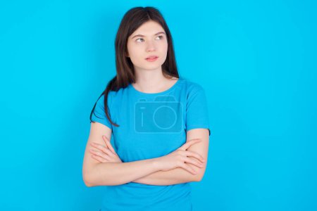 Téléchargez les photos : Charmante jeune fille caucasienne réfléchie portant T-shirt bleu isolé sur fond bleu se tient avec les bras repliés concentrés quelque part avec expression coûteuse pense quoi faire - en image libre de droit