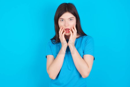 Photo for Speechless young caucasian girl wearing blue T-shirt isolated over blue background keeps hands near opened mouth reacts to shocking news stares wondered at camera - Royalty Free Image