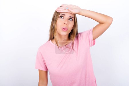 Young Caucasian girl wearing pink T-shirt on white background wiping forehead with hand making phew gesture, expressing relief feels happy that he prevented huge disaster. It was close enough