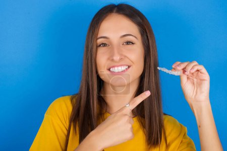 Téléchargez les photos : Jeune femme tenant un aligneur invisible et le pointant du doigt. Concept de soins dentaires et de confiance. - en image libre de droit