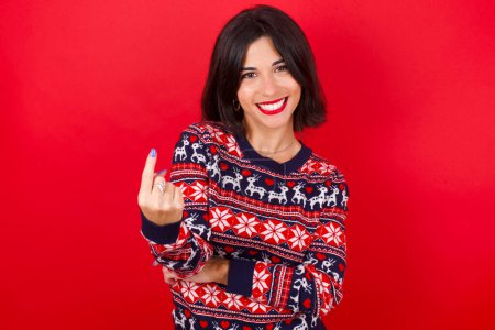 Téléchargez les photos : Brune caucasienne femme portant chandail de Noël sur fond rouge Beckoning venir ici geste avec la main invitant accueillant heureux et souriant - en image libre de droit