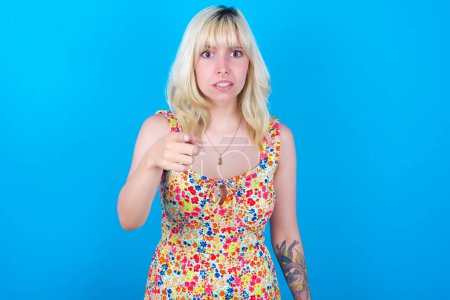 Photo for Shocked caucasian girl wearing floral dress isolated over blue background points at you with stunned expression - Royalty Free Image