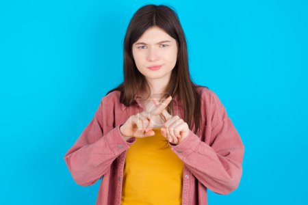 Photo for Young caucasian girl wearing pink shirt isolated over blue background has rejection angry expression crossing fingers doing negative sign. - Royalty Free Image
