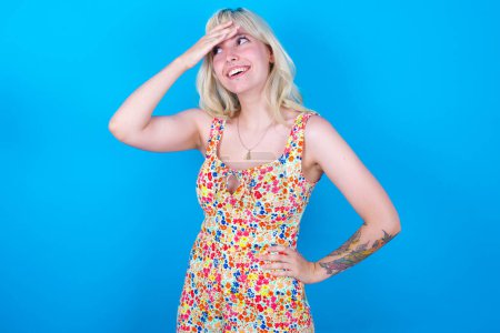Photo for Caucasian girl wearing floral dress isolated over blue background touching forehead, hears something surprising, glad receive good news, feels relieved. Almost got in trouble. - Royalty Free Image