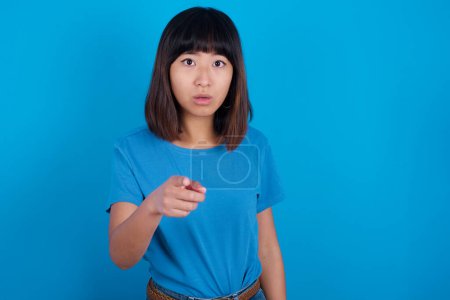 Photo for Shocked young asian woman wearing t-shirt against blue background points at you with stunned expression - Royalty Free Image