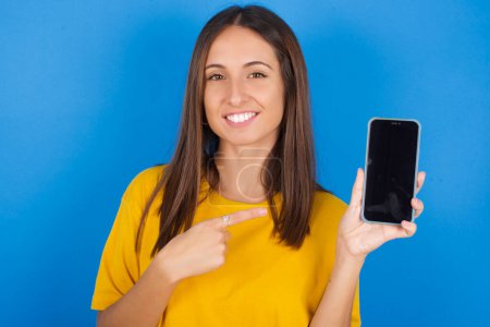 Photo for Smiling beautiful young woman showing and pointing at empty phone screen. Advertisement and communication concept. - Royalty Free Image