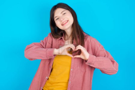 Photo for Young caucasian girl wearing pink shirt isolated over blue background smiling in love showing heart symbol and shape with hands. Romantic concept. - Royalty Free Image