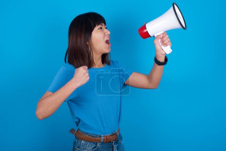 Photo for Young asian woman wearing t-shirt against blue background communicates shouting loud holding a megaphone, expressing success and positive concept, idea for marketing or sales. - Royalty Free Image