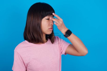 Foto de Muy molesto joven mujer asiática usando camiseta sobre fondo azul tocando la nariz entre los ojos cerrados, quiere llorar, tener una relación estresante o tener problemas con el trabajo - Imagen libre de derechos