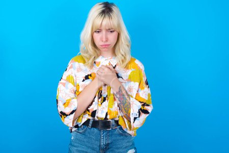 Photo for Sad caucasian girl wearing floral shirt isolated over blue background feeling upset while spending time at home alone staring at camera with unhappy or regretful look. - Royalty Free Image