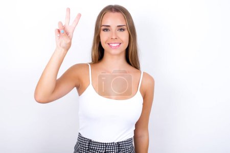 Photo for Young Caucasian girl wearing white tank top on white background showing and pointing up with fingers number two while smiling confident and happy. - Royalty Free Image