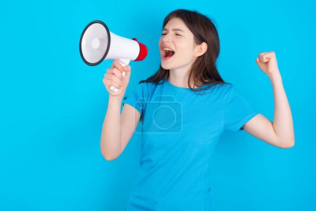 Photo for Young caucasian girl wearing blue T-shirt isolated over blue background communicates shouting loud holding a megaphone, expressing success and positive concept, idea for marketing or sales. - Royalty Free Image
