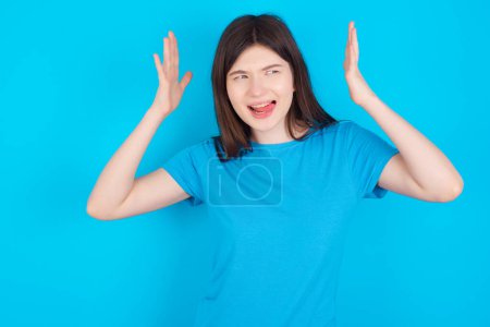 Foto de Joven caucásico chica usando azul camiseta aislado sobre azul fondo se vuelve loco como cabeza va alrededor se siente estresado debido a horrible situación - Imagen libre de derechos