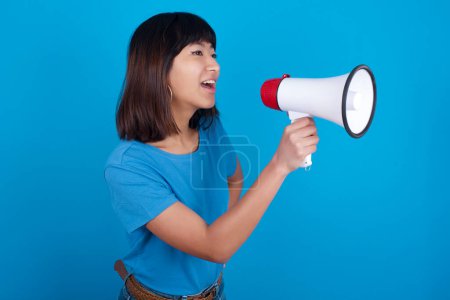 Photo for Funny young asian woman wearing t-shirt against blue background People sincere emotions lifestyle concept. Mock up copy space. Screaming in megaphone. - Royalty Free Image