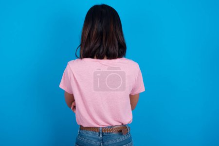 Photo for Young asian woman wearing t-shirt against blue background standing backwards looking away with arms on body. - Royalty Free Image