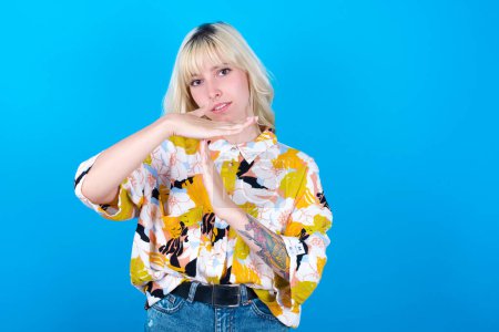 Photo for Caucasian girl wearing floral shirt isolated over blue background feels tired and bored, making a timeout gesture, needs to stop because of work stress, time concept. - Royalty Free Image