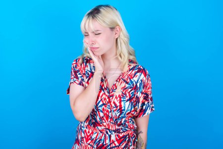 Photo for Caucasian girl wearing floral dress isolated over blue background with toothache - Royalty Free Image