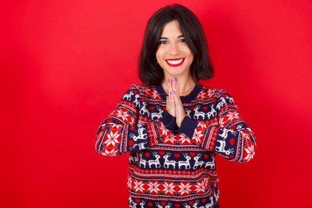 Téléchargez les photos : Brune caucasienne femme portant chandail de Noël sur fond rouge priant avec les mains ensemble demandant pardon souriant confiant. - en image libre de droit