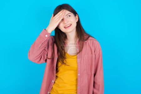 Photo for Young caucasian girl wearing pink shirt isolated over blue background touching forehead, hears something surprising, glad receive good news, feels relieved. Almost got in trouble. - Royalty Free Image