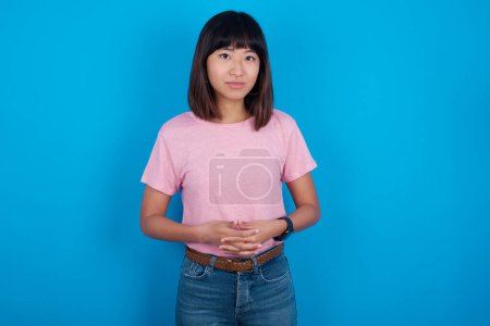 Téléchargez les photos : Business Concept - Portrait de jeune femme asiatique portant un t-shirt sur fond bleu tenant la main avec un visage confiant. - en image libre de droit