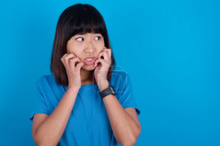 Téléchargez les photos : Terrifié jeune asiatique femme porter t-shirt sur fond bleu semble vide espace maison seul nuit sans lune - en image libre de droit