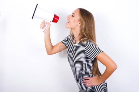 Photo for Funny beautiful blonde girl wearing striped t-shirt on white background People sincere emotions lifestyle concept. Mock up copy space. Screaming in megaphone. - Royalty Free Image