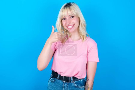 Foto de Chica caucásica con camiseta rosa aislado sobre fondo azul dando el pulgar hacia arriba gesto, buen trabajo! Emoción humana positiva expresión facial lenguaje corporal. - Imagen libre de derechos