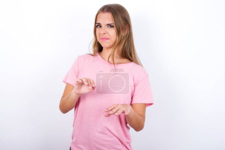 Ugh how disgusting! Displeased Young Caucasian girl wearing pink T-shirt on white background has dissatisfied facial expression as sees something abominable.