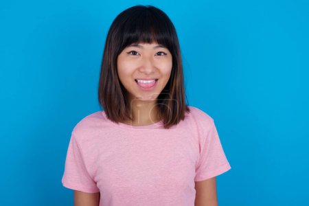 Foto de Joven asiático mujer usando t-shirt contra azul fondo con feliz y divertido cara sonriendo y mostrando lengua. - Imagen libre de derechos
