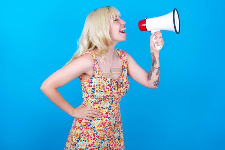 Photo for Funny caucasian girl wearing floral dress isolated over blue background People sincere emotions lifestyle concept. Mock up copy space. Screaming in megaphone. - Royalty Free Image