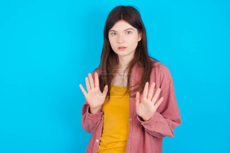 Photo for Young caucasian girl wearing pink shirt isolated over blue background doing stop sing with palm of the hand. Warning expression with negative and serious gesture on the face. - Royalty Free Image