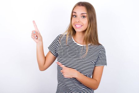 Foto de Hermosa chica rubia con camiseta a rayas en los puntos de fondo blanco en el espacio de copia indica para la publicidad da la dirección correcta - Imagen libre de derechos