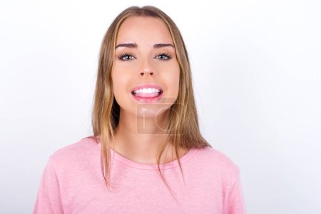 Téléchargez les photos : Jeune fille caucasienne portant un t-shirt rose sur fond blanc avec un visage heureux et drôle souriant et montrant la langue. - en image libre de droit