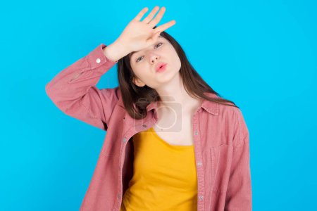Photo for Young caucasian girl wearing pink shirt isolated over blue background wiping forehead with hand making phew gesture, expressing relief feels happy that he prevented huge disaster. It was close enough - Royalty Free Image