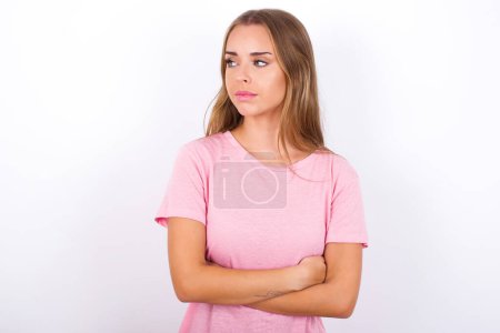 Téléchargez les photos : Plaisir jeune fille caucasienne portant T-shirt rose sur fond blanc garde les mains croisées sur la poitrine semble heureusement de côté - en image libre de droit