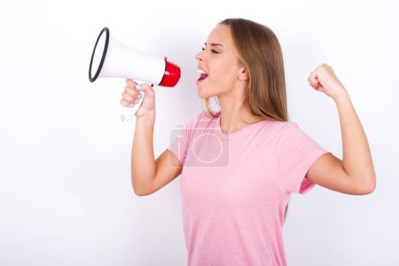 Photo for Young Caucasian girl wearing pink T-shirt on white background communicates shouting loud holding a megaphone, expressing success and positive concept, idea for marketing or sales. - Royalty Free Image