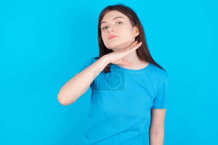 Foto de Joven chica caucásica vistiendo camiseta azul aislada sobre fondo de estudio azul cortando garganta con la mano como cuchillo, amenazan la agresión con violencia furiosa. - Imagen libre de derechos