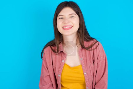 Téléchargez les photos : Jeune fille caucasienne portant chemise rose isolé sur fond bleu avec visage heureux et drôle souriant et montrant la langue. - en image libre de droit