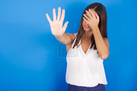 Photo for Beautiful young woman covers eyes with palm and doing stop gesture, tries to hide. Don't look at me, I don't want to see, feels ashamed or scared. - Royalty Free Image