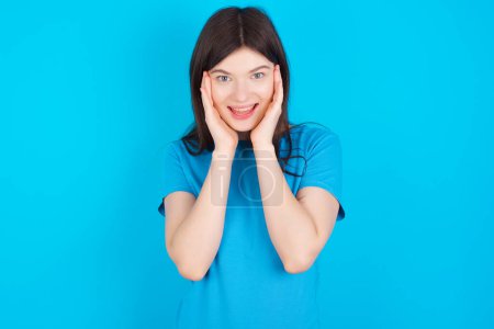Téléchargez les photos : Jeune fille caucasienne portant t-shirt bleu isolé sur fond studio bleu regardant gai. Concept de réaction heureuse - en image libre de droit