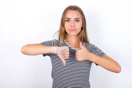 Photo for Beautiful blonde girl wearing striped t-shirt on white background showing thumb up down sign - Royalty Free Image
