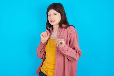 Photo for Ugh how disgusting! Displeased young caucasian girl wearing pink shirt isolated over blue background has dissatisfied facial expression as sees something abominable. - Royalty Free Image