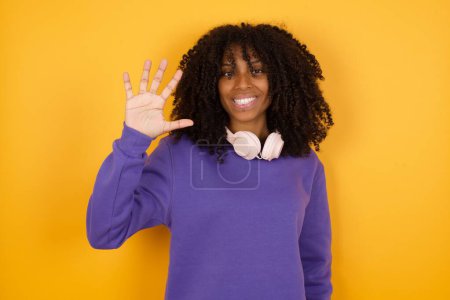 Photo for Portrait of young expressive african american woman with headphones on yellow background showing five fingers - Royalty Free Image