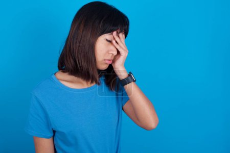 Foto de Joven mujer asiática vistiendo camiseta azul sobre fondo azul con expresión triste cubriendo la cara con las manos mientras llora. Concepto de depresión. - Imagen libre de derechos