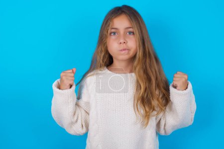Photo for Irritated pretty teen girl blows cheeks with anger and raises clenched fists expresses rage and aggressive emotions. Furious model - Royalty Free Image